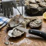 L'Écaill'Art posé sur une huître ouverte avec citron et bol d'ail