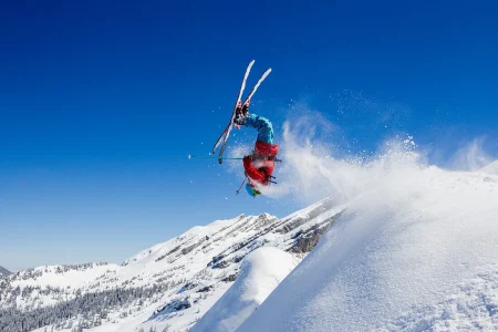 Skieur faisant un salto arrière avec des montagnes enneigées autour